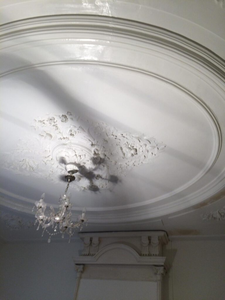 Gerestaureerd plafond met elegante ornamenten en kroonluchter door Elviservices.
