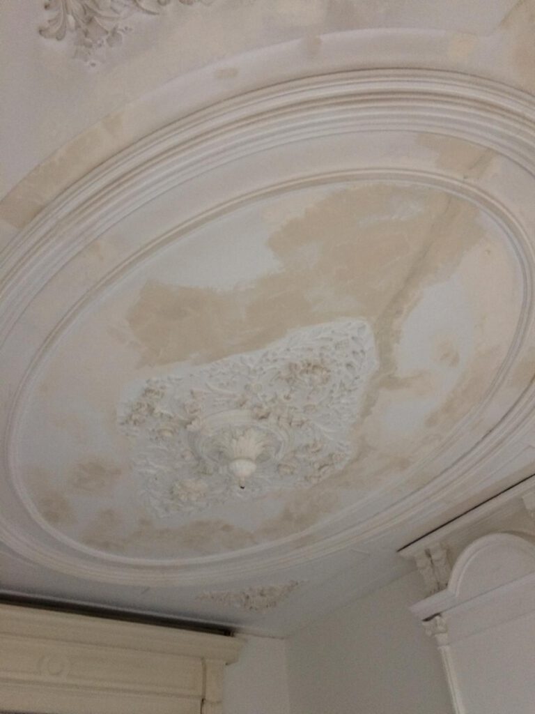 Plafond in restauratiefase met beschadigde ornamenten, voorbereid door Elviservices.